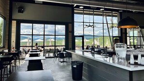En moderne restaurant med store vinduer der giver udsigt til bjergene, et barområde med vanddispenser og et rent, industrielt indretning.