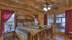Ein Schlafzimmer einer Holzhütte mit einem Bett, einem Deckenventilator und Blick ins Freie.