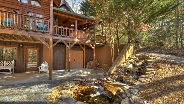 Eine Holzhütte mit Balkon, einem Steinweg und einem kleinen Wasserfall.