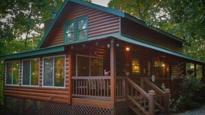 A log cabin with a porch, large windows, and a staircase leading to the entrance.