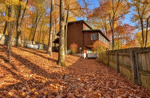 Une cabane aux murs en bois, entourée d’arbres aux feuilles d’automne, et une clôture en bois.