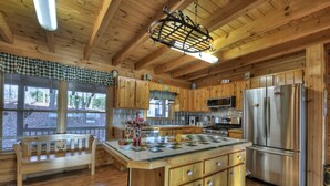 A wooden cabin kitchen with a large island, wooden cabinets, a refrigerator, and a bench by the window.