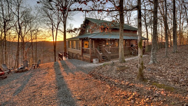 A rustic cabin with a porch, surrounded by trees, and a gravel path leading to it.