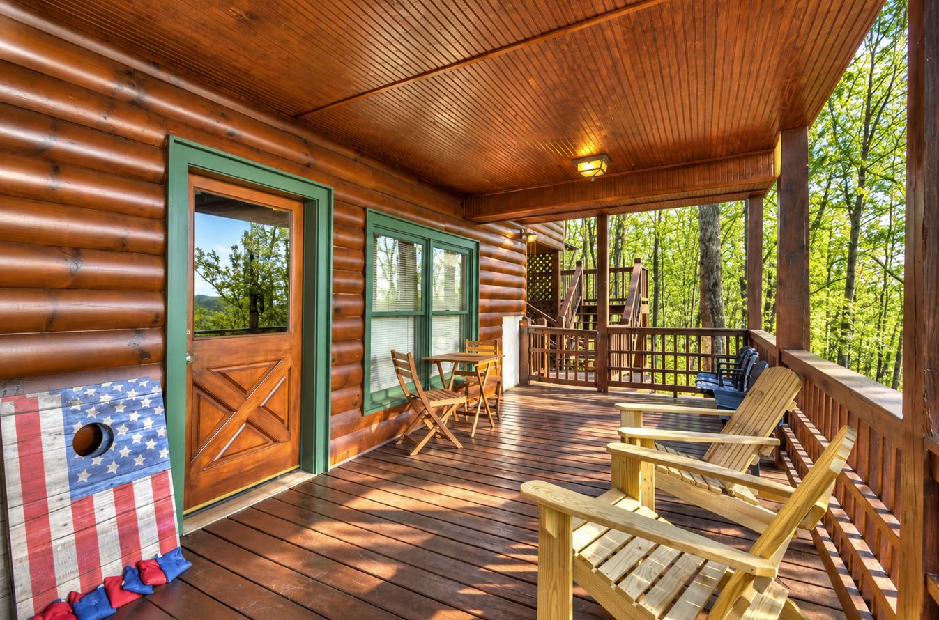 A wooden deck with Adirondack chairs, a covered porch, and a view of the forest.