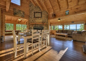 L’intérieur d’un chalet en bois est doté d’une cheminée en pierre, d’un coin repas et d’un canapé placé face à de grandes fenêtres.