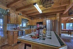 A wooden cabin kitchen with a central island, wooden cabinets, a refrigerator, a microwave, and a sink. - Discover Treetop Getaway -Pet-friendly retreat with panoramic mountain views, hot tub, firepit, fenced yard, WiFi, and a game-room (Ellijay)