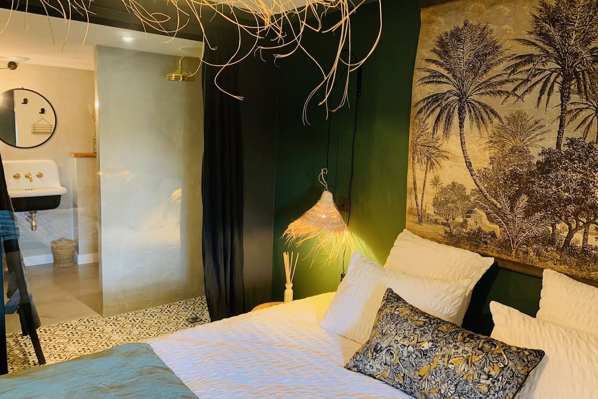A bedroom with a bed, a hanging light fixture, a wall-mounted sink, and a tropical mural.