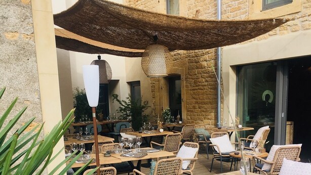 An outdoor dining area with wicker chairs and tables, surrounded by greenery and a stone building. - La Cambrousse (Villers-la-Chèvre)