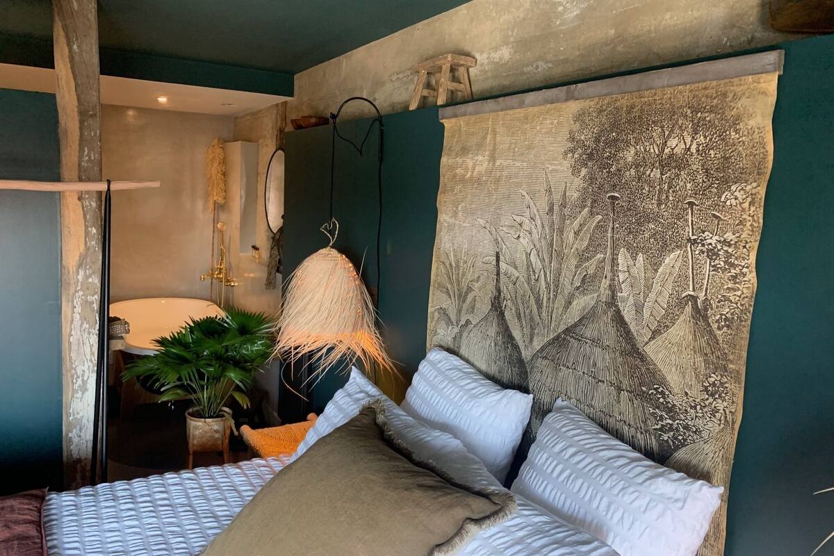 A bedroom with a large bed, a hanging lamp, and a wall-mounted artwork.