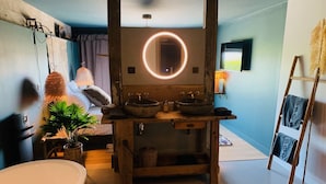 A bathroom with a wooden vanity, a large mirror with a circular light, a bathtub, and a towel rack. - La Cambrousse (Villers-la-Chèvre)