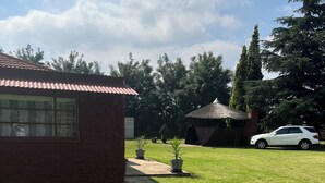 A grassy yard with a building, a car, and a thatched-roof structure. - Captivating 1-bed Studio in Springs (Springs)