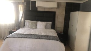 A neatly made bed with white linens and a patterned throw, a bedside table with a lamp, and a wardrobe against the wall. - Captivating 1-bed Studio in Springs (Springs)