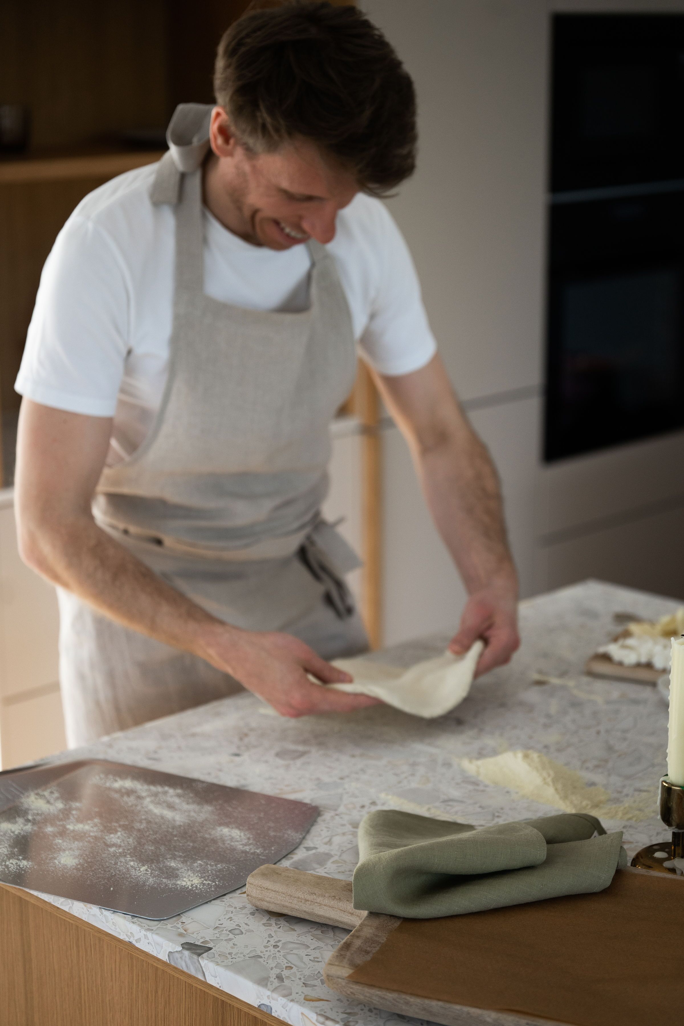 A person in a kitchen preparing dough on a countertop with a rolling pin, a baking sheet, and a rolling pin nearby.