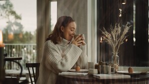 A person sitting at a table with a cup, a vase with dried flowers, and a candle. - Hilltop Forest (Inga)
