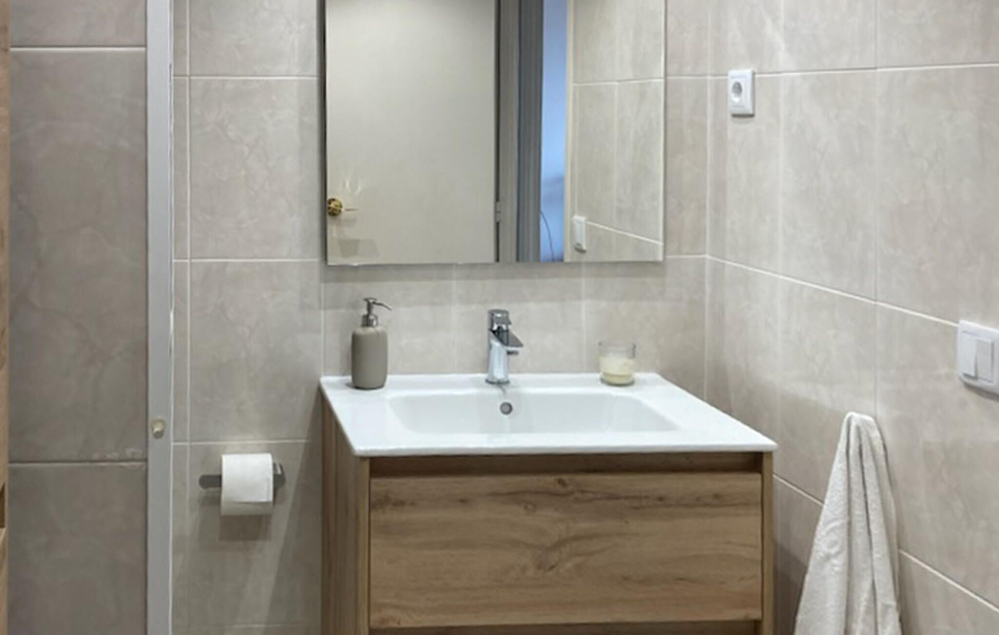 Un baño con un lavabo blanco, tocador de madera, un espejo y una toalla colgada en la pared.