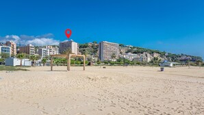 Een strand met een kiosk, palmbomen en gebouwen op de achtergrond.