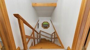 A wooden staircase with a handrail, leading to a room with white walls and a window with a green view. - Bear Essentials Lakefront Hideaway (Huntsville)