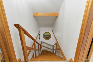 Eine Holztreppe mit Handlauf, die zu einem Zimmer mit weißen Wänden und einem Fenster mit Grünblick führt.