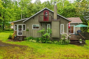A two-story house with a balcony, a chimney, and a porch with a green umbrella.