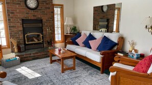 A cozy living room with a fireplace, a sofa with cushions, a coffee table, and a wooden chair. - Bear Essentials Lakefront Hideaway (Huntsville)