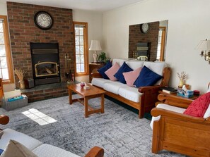 A cozy living room with a fireplace, a sofa with cushions, a coffee table, and a wooden chair.