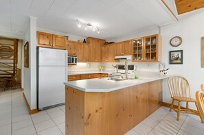 A kitchen with wooden cabinets, a white refrigerator, a sink, and a dining area with chairs.