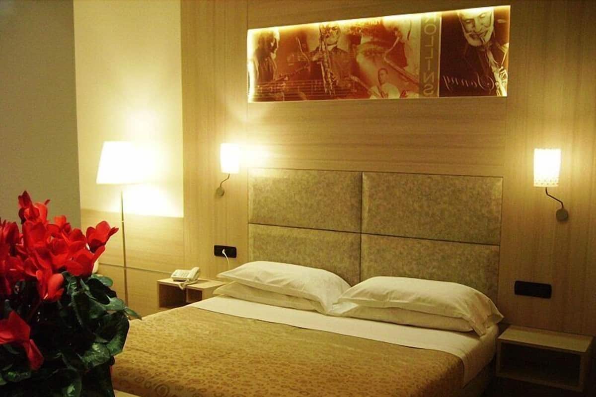 Habitación de hotel con una cama grande, dos lámparas de noche, una mesita de noche y un cartel en la pared.