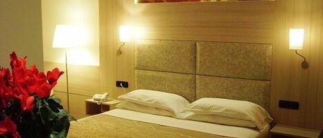 A hotel room with a large bed, two bedside lamps, a nightstand, and a wall-mounted poster.