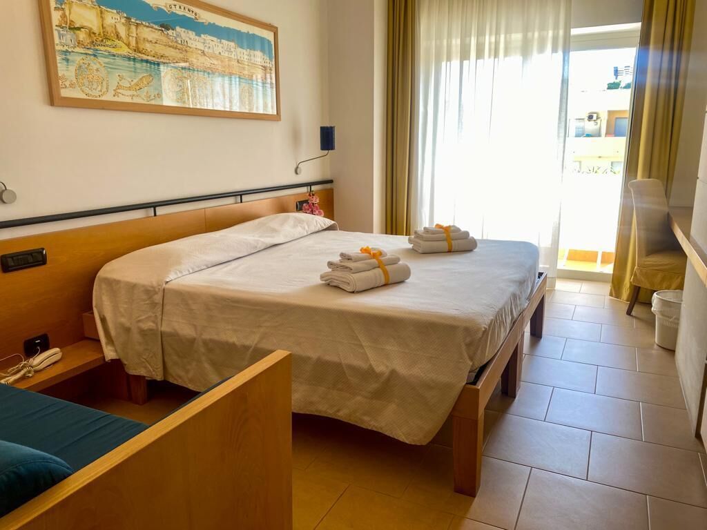 Une chambre d’hôtel avec deux lits, une tête de lit en bois, un tableau au mur et une vue sur l’extérieur par la fenêtre.