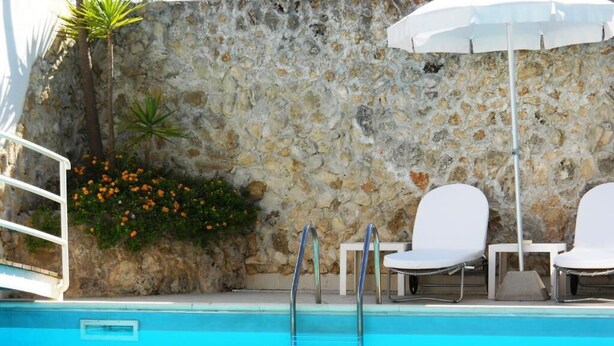 Ein Pool mit weißen Liegestühlen und einer Steinsäule.