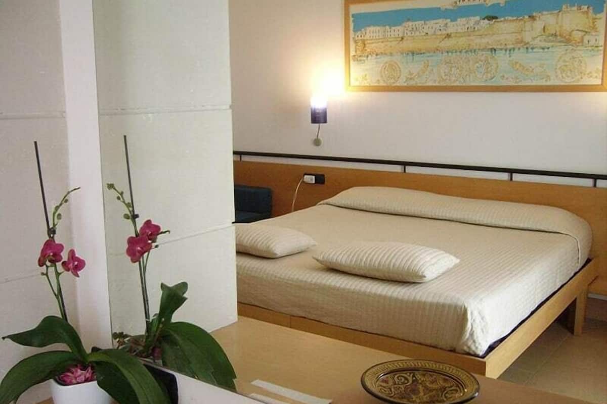 Un dormitorio con una cama, almohadas, una mesita de noche, un plato decorativo y un cuadro colgado en la pared.