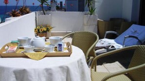 Ein Balkon mit einem Frühstückstisch, Korbstühlen und Blick auf das Meer und Gebäude.