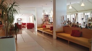 Eine großzügige Lobby mit modernem Design, mit einer zentralen Sitzecke mit roten und beigen Sofas, einer großen Topfpflanze und einer Wand mit vertikalen Elementen.