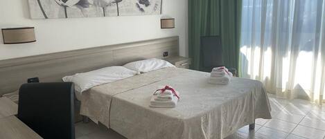 Habitación de hotel con cama, escritorio, silla, un cuadro en la pared y ventana con cortinas.