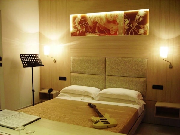 Habitación de hotel con cama, una guitarra, un atril y una lámpara fijada a la pared.