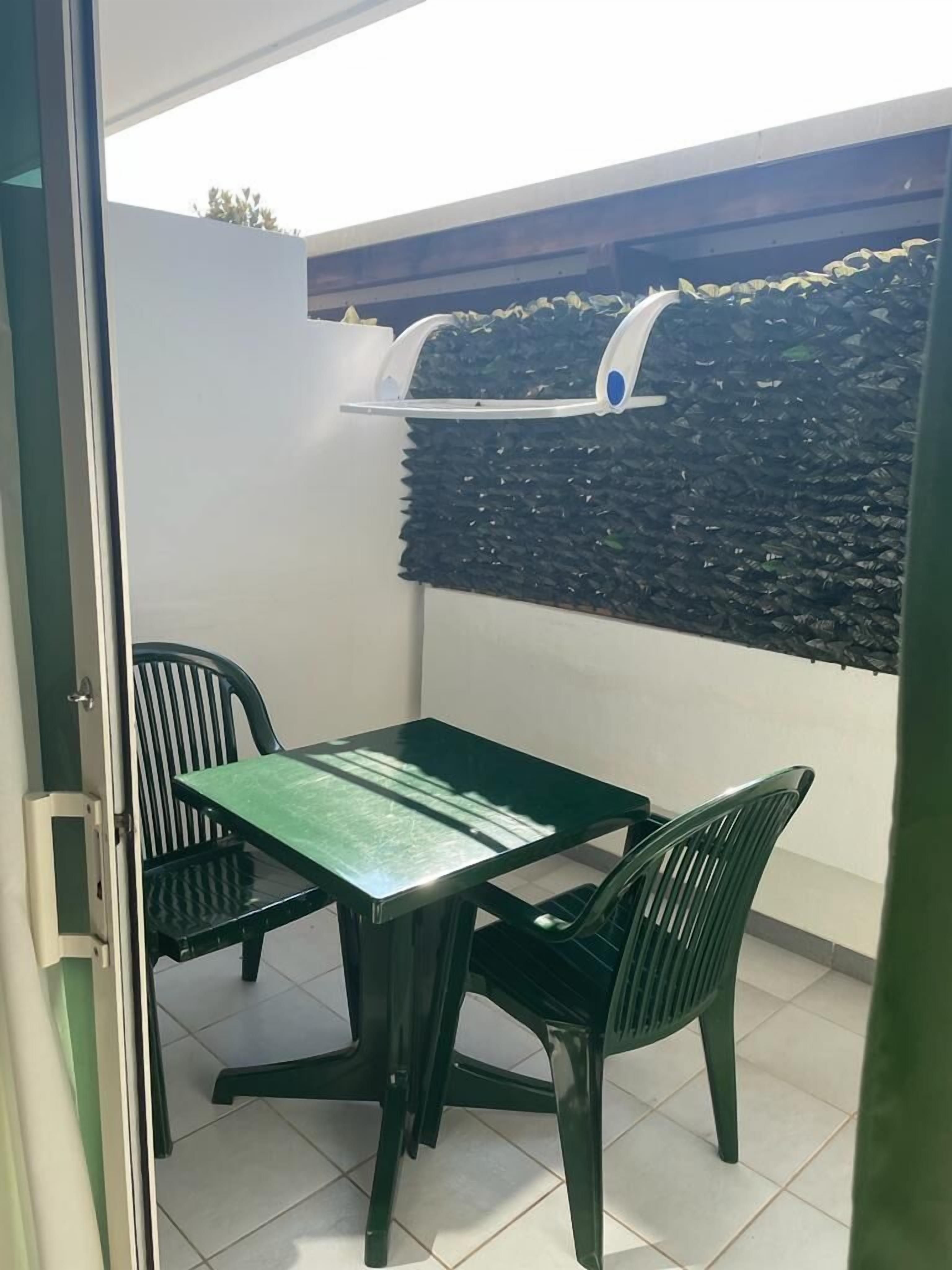 Un pequeño patio con mesa y sillas, una parrilla y un muro con superficie texturizada.