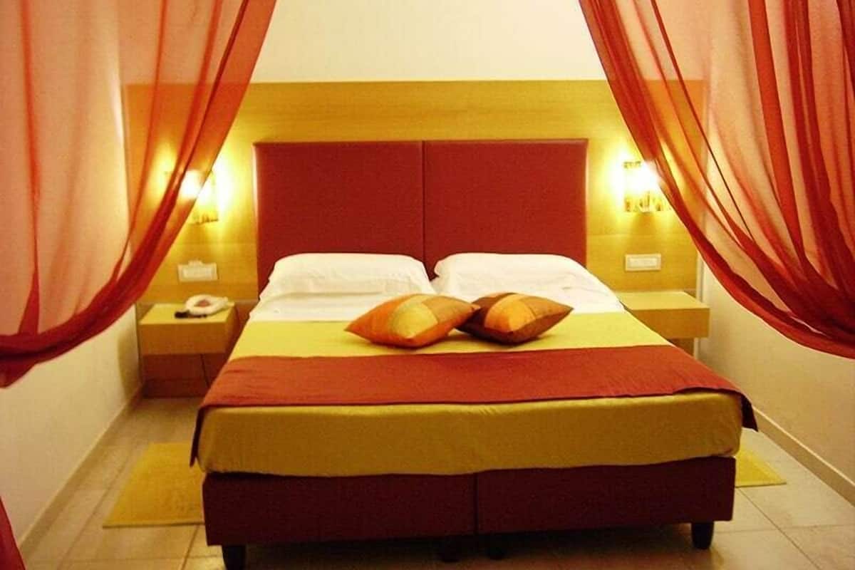 Una cama con cabecera roja, dos almohadas y una colcha amarilla. Hay dos mesitas de noche con lámparas.
