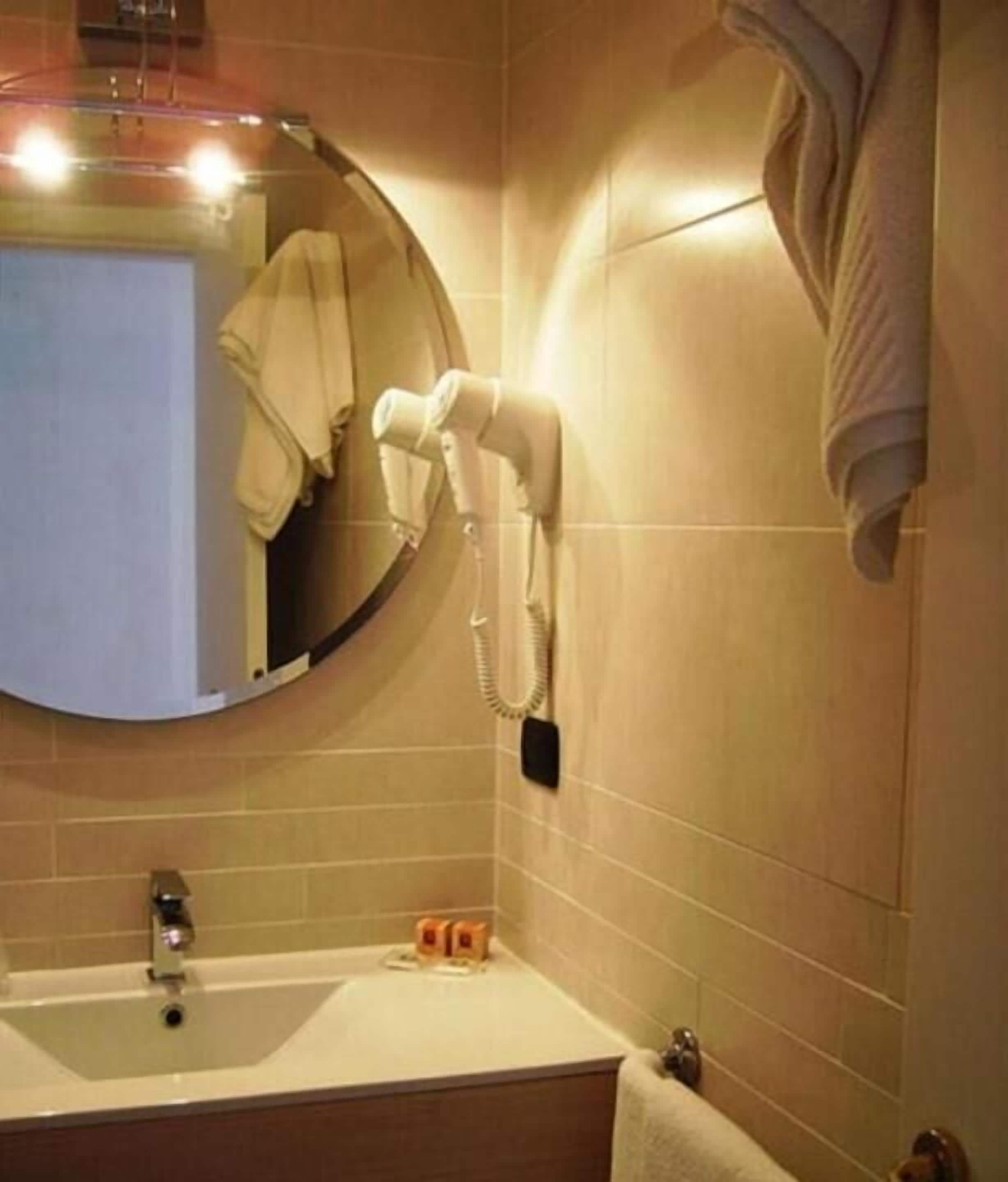 Une salle de bain équipée d’un lavabo, d’un miroir, d’un sèche-cheveux et d’une serviette accrochée au mur.