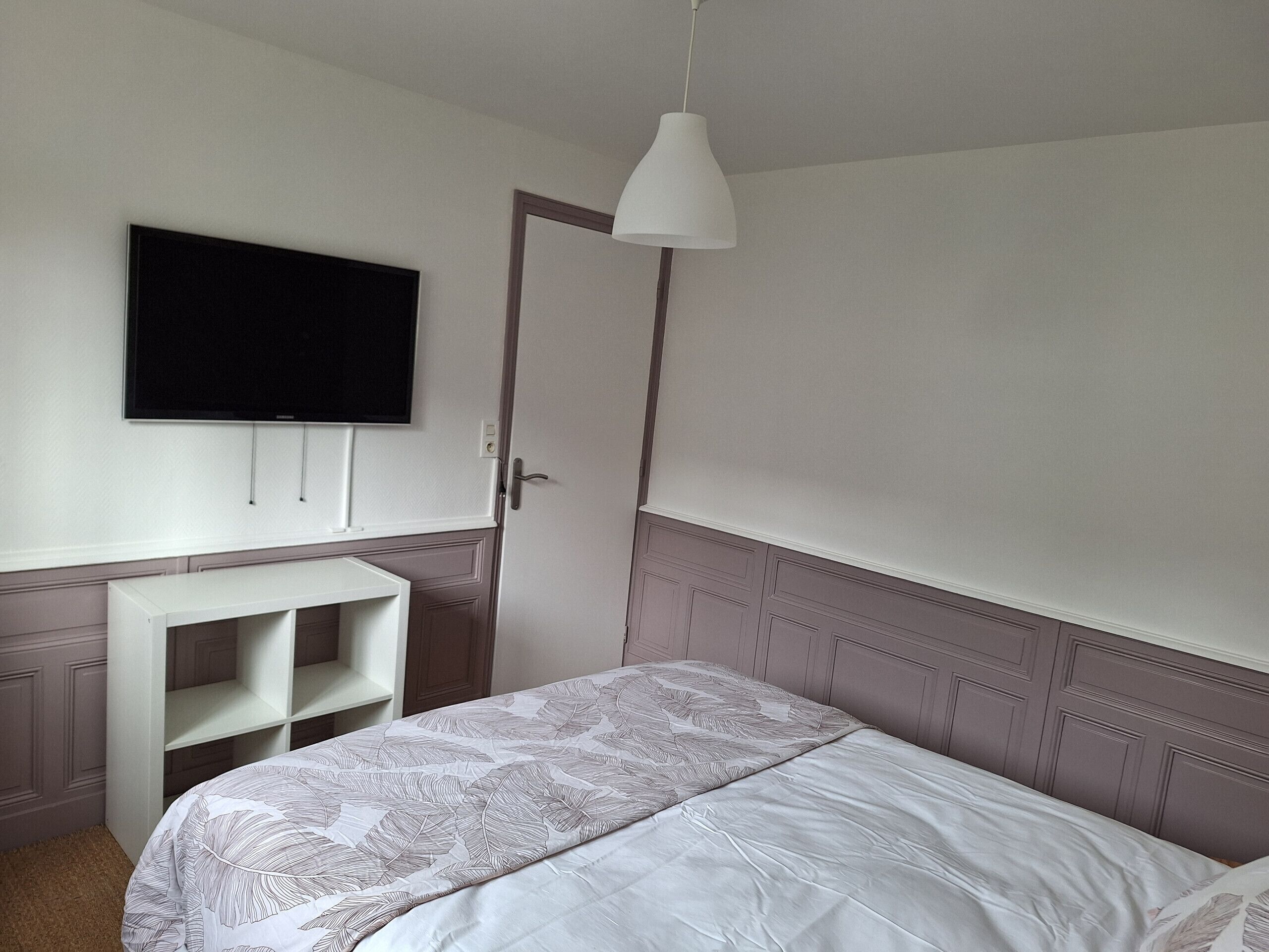 Une chambre à coucher avec un lit, un téléviseur fixé au mur, un bureau et une porte.