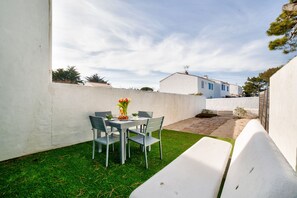 Une terrasse avec une table et des chaises, un petit jardin et un bâtiment blanc en arrière-plan.