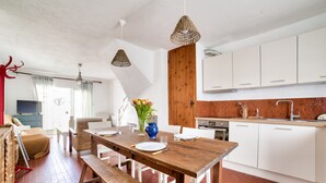 Una cocina moderna con armarios blancos, una mesa de comedor de madera y lámparas colgantes de mimbre.