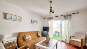 Una sala de estar con sofá, dos sillones, una mesita de centro, televisor y una ventana con cortinas.