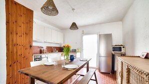 Una cocina con una mesa de madera, armarios blancos, un refrigerador y una separador de mimbre.