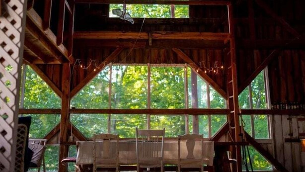 Un intérieur rustique en bois, avec une grande fenêtre donnant sur une forêt. On aperçoit un banc en bois et une chaise au premier plan.