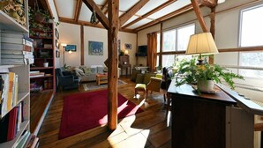 Un salon chaleureux avec des poutres en bois, un tapis rouge, une bibliothèque, un canapé et une table sur laquelle se trouvent une lampe et des plantes.