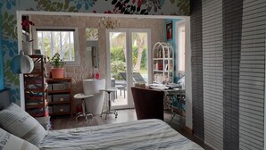 A bedroom with a bed, a desk, a chair, a bookshelf, a potted plant, a bathroom with a sink and mirror, and a window with a view of greenery. - Villa Les Palmiers, 15 minutes from Monaco, Nice and the seaside. (Èze)