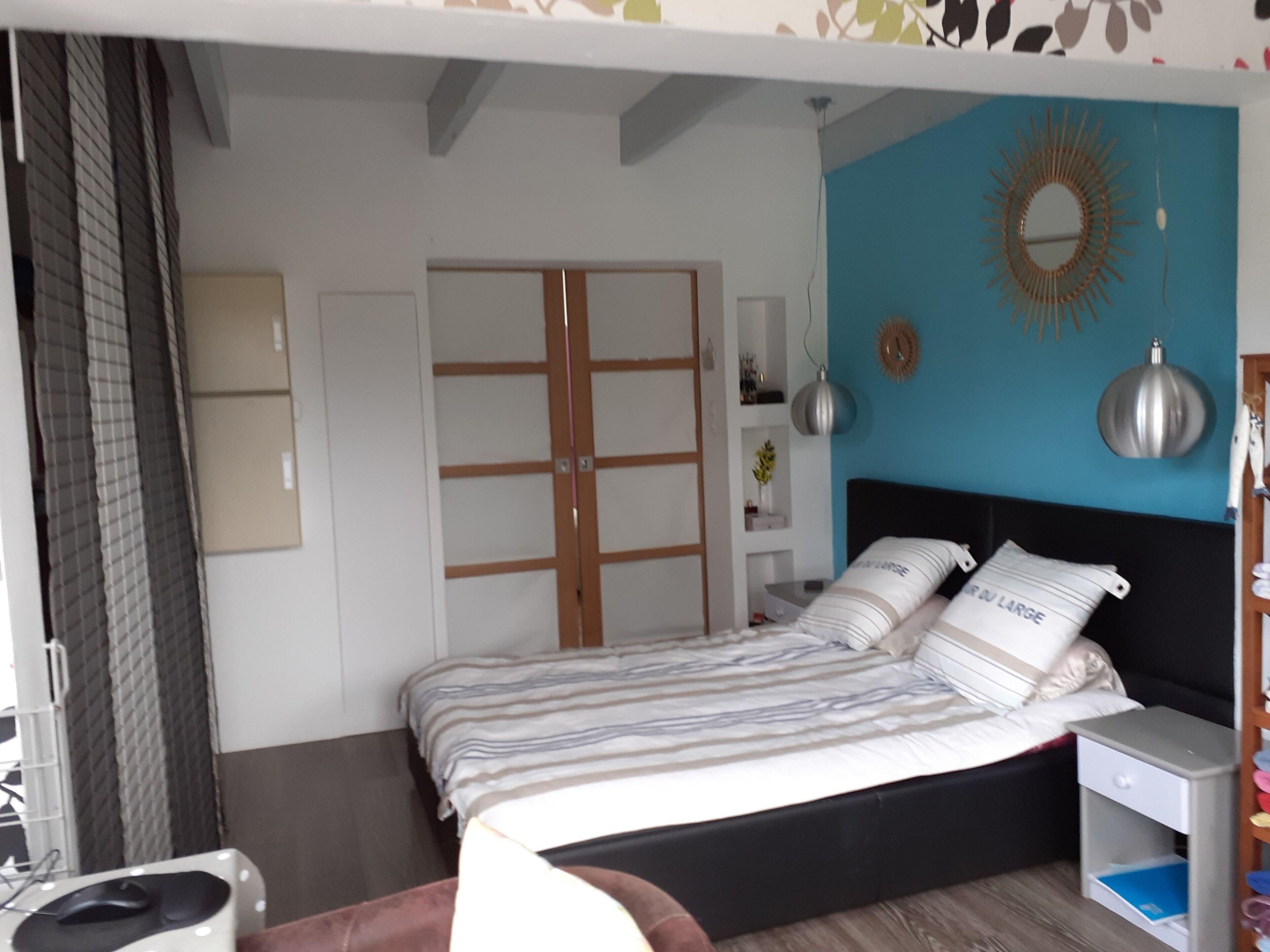 A bedroom with a bed, bedside table, wardrobe, and a mirror on the wall.