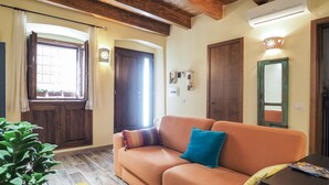 A living room with a sofa, a small table, a potted plant, and a window with curtains. - Domu Mea - Morada - Two Bedroom House, Sleeps 4 (Iglesias)