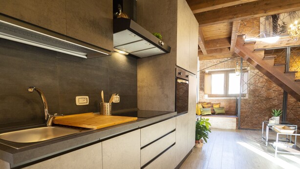 Een moderne keuken met een groot eiland, donkere tegels en een houten trap naar een vide.