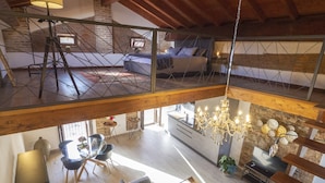 Een ruime loft met een hoge plafond, zichtbare houten balken, een eethoek met een glazen tafel en stoelen, een keuken met moderne apparatuur en een kroonluchter.